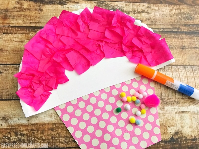 Decorating a paper plate cupcake craft with pom poms